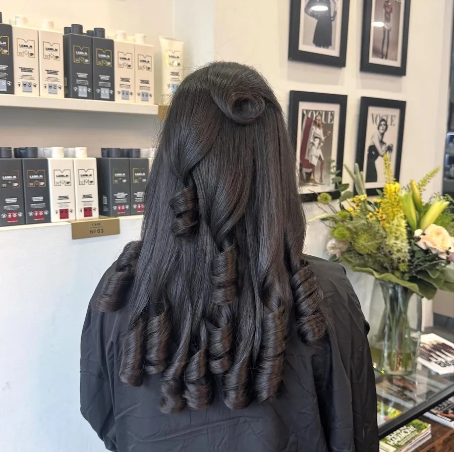 Dark hair half up, finished in a glossy curly blow-dry